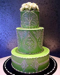 Round three tier green wedding cake decorated with intricate and elaborate white artwork