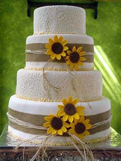 Four tier round white and straw wedding cake decorated with handcrafted yellow sunflowers
