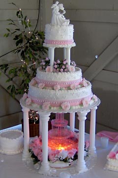 Three tier white buttercream wedding cake hoisted up on pillars to cater for a glorious water fountain