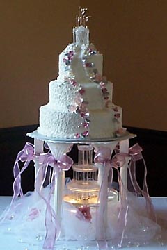 Three tier pink and white castle wedding cake raised up on 5 pillars to allow a wedding cake fountain underneath