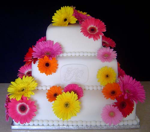 Three iter square fondant wedding cake decorated with pink, yellow, orange and red gerbera daisies