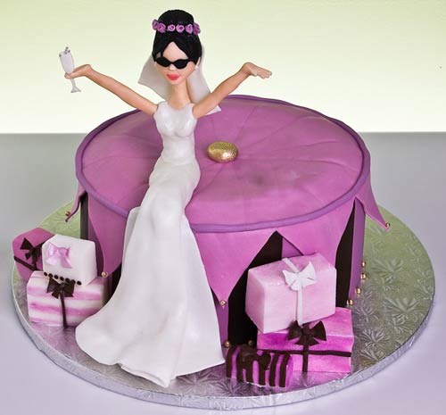 Novelty, round purple bridal shower cake with a bride wedding cake topper. Decorated with small and purple and pink wedding gifts