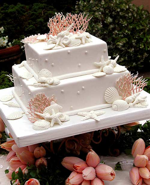 Stunning two tier white wedding cake decorated with orange coral, white edible seashells