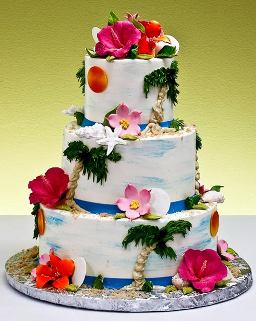 Three tier white and blue Hawiian wedding cake decorated with hand painted palm trees, sea shells and an air brushed blue sky