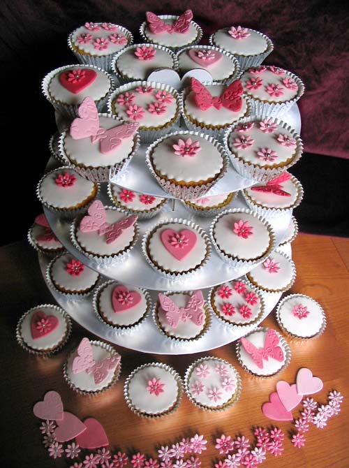 A cupcake tiered wedding cake arrangement. An assortment of cupcakes, decorated with either pink hearts, pink butterflies or pink sugar flowers