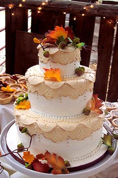 Romantic, three tier, white and beige, lacy wedding cake decorated with green, orange and yellow autumn leaves