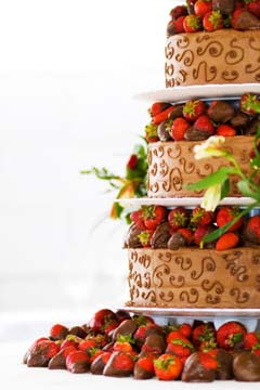 three tier chocolate strawberries wedding cake placed on platforms layers. Each tier is decorated with chocolate dipped strawberries